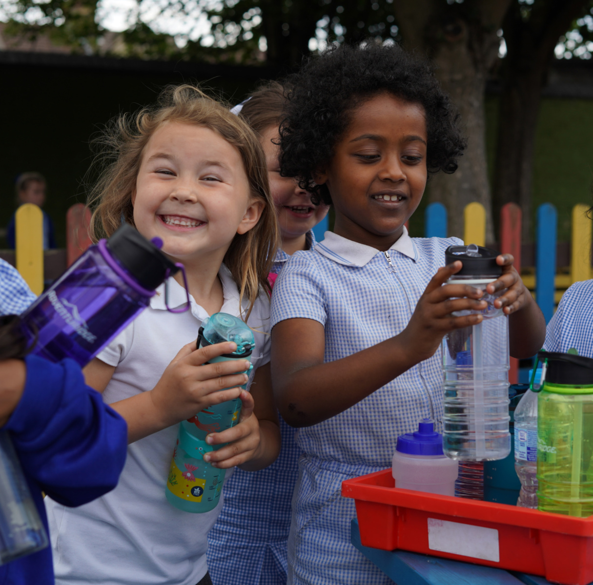 Two young girls are pictured wearing their academy uniform and smiling for the camera outdoors, whilst filling up their water bottles.