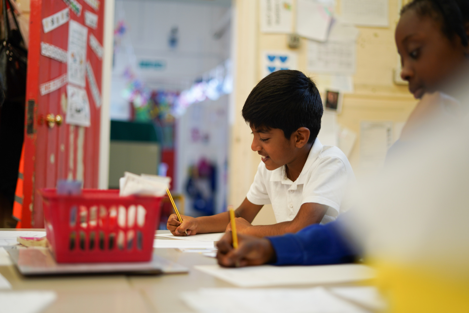 A young boy is seen sat at his desk, wearing his academy uniform with a bright smile on his face and focusing on his work.