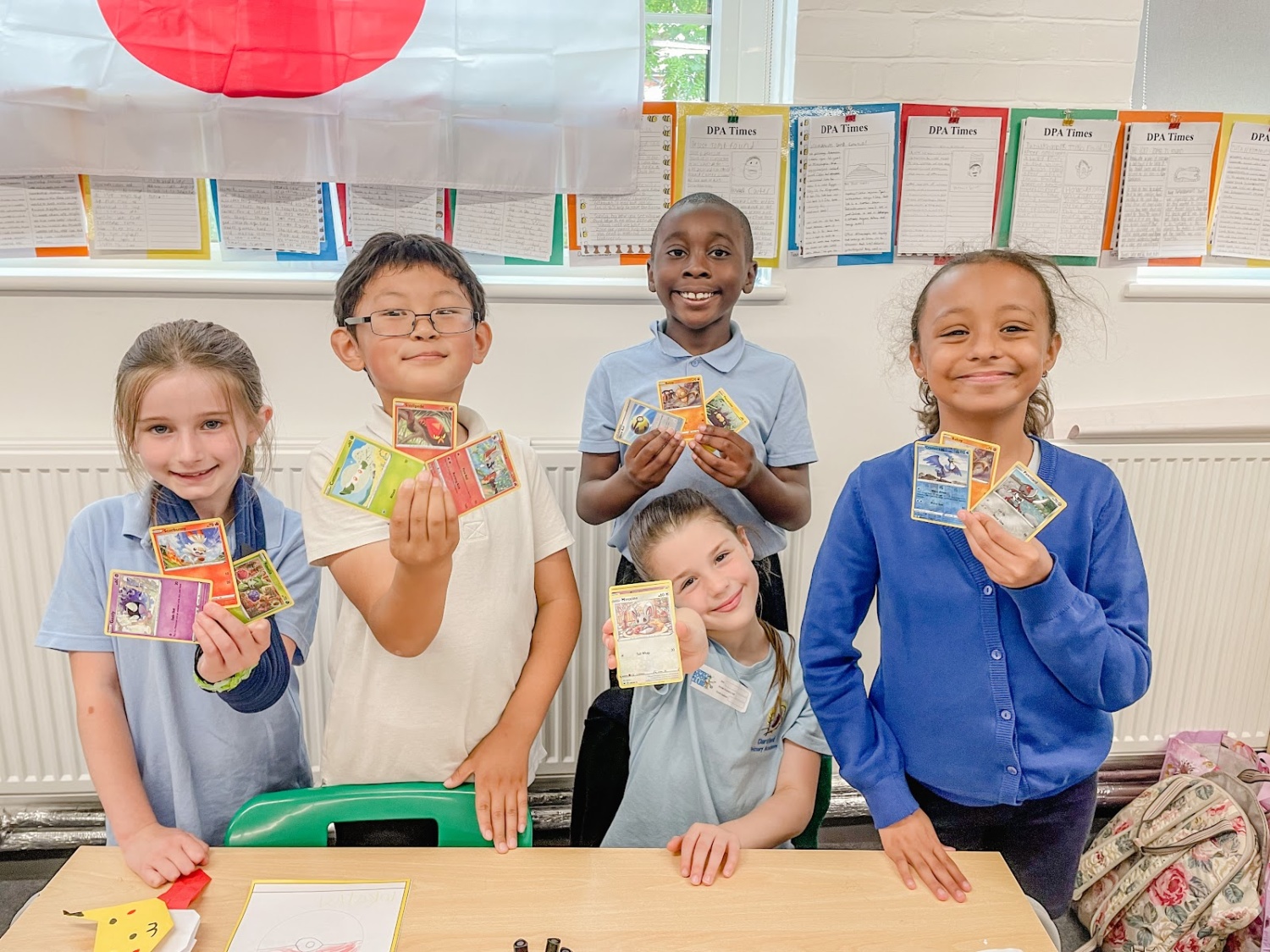 A group of five pupils are pictured smiling together for the camera, holding up some Pokemon cards they have been playing with.