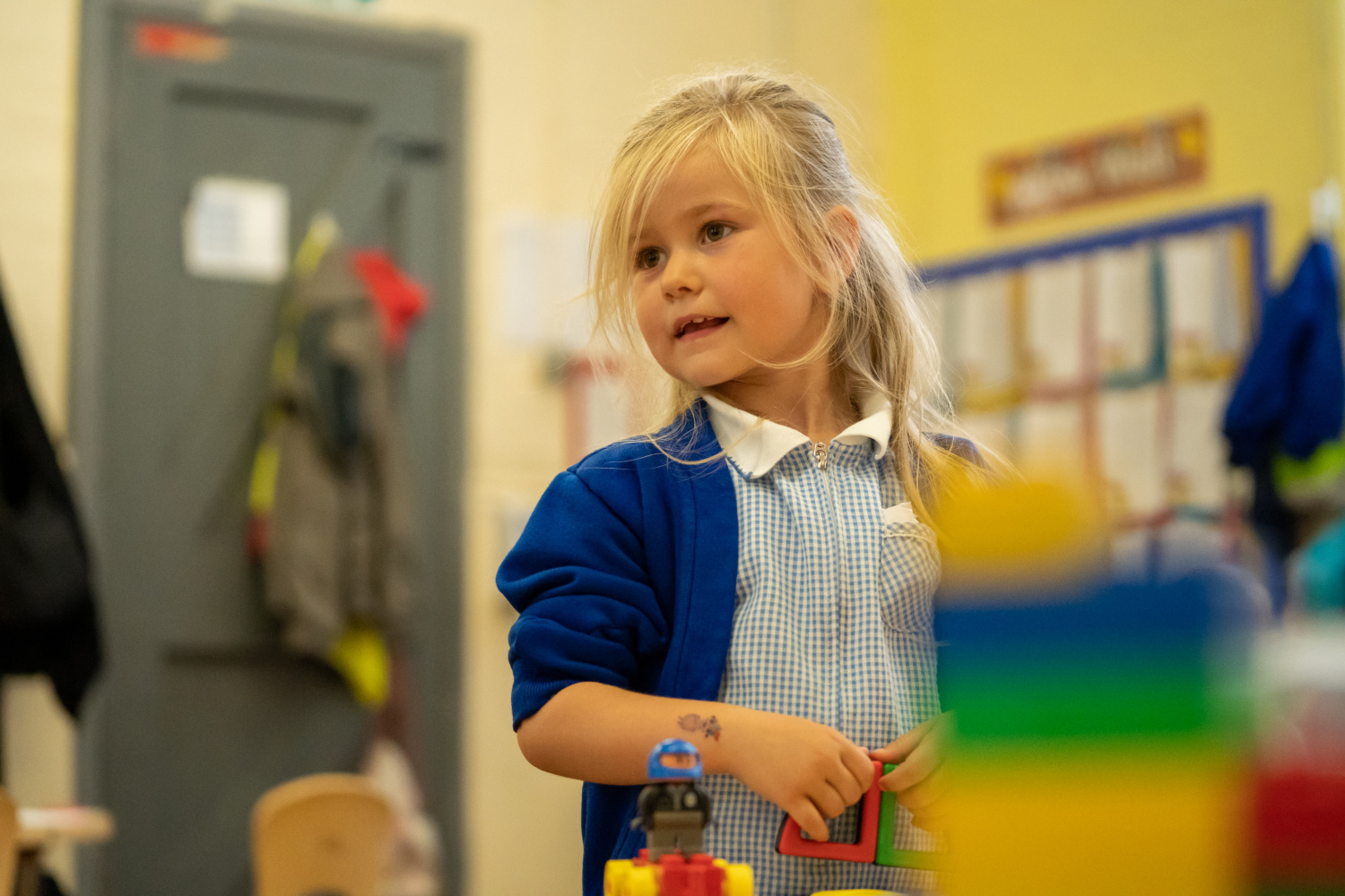 A young girl is seen wearing her academy uniform and playing with some LEGO in a classroom.