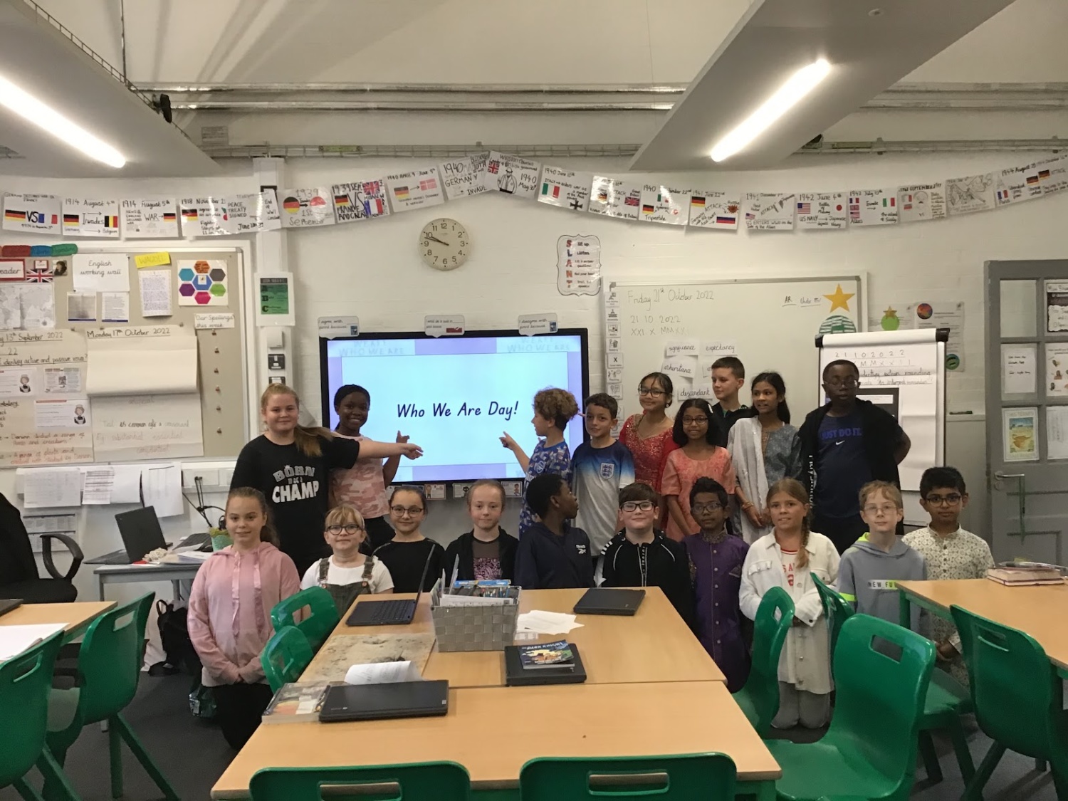 A class of pupils are pictured smiling for the camera together at the front of the class, after giving a presentation called 'Who We Are Day'.