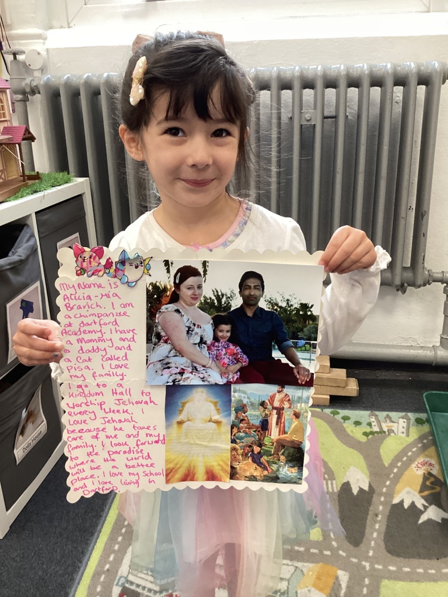 A young girl is seen smiling for the camera whilst holding up some work she has created about a subject.