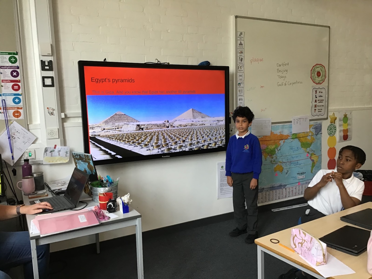 A young boy in academy uniform is pictured standing beside an Interactive Board at the front of the classroom, about to deliver a presentation on Egypt's Pyramids.