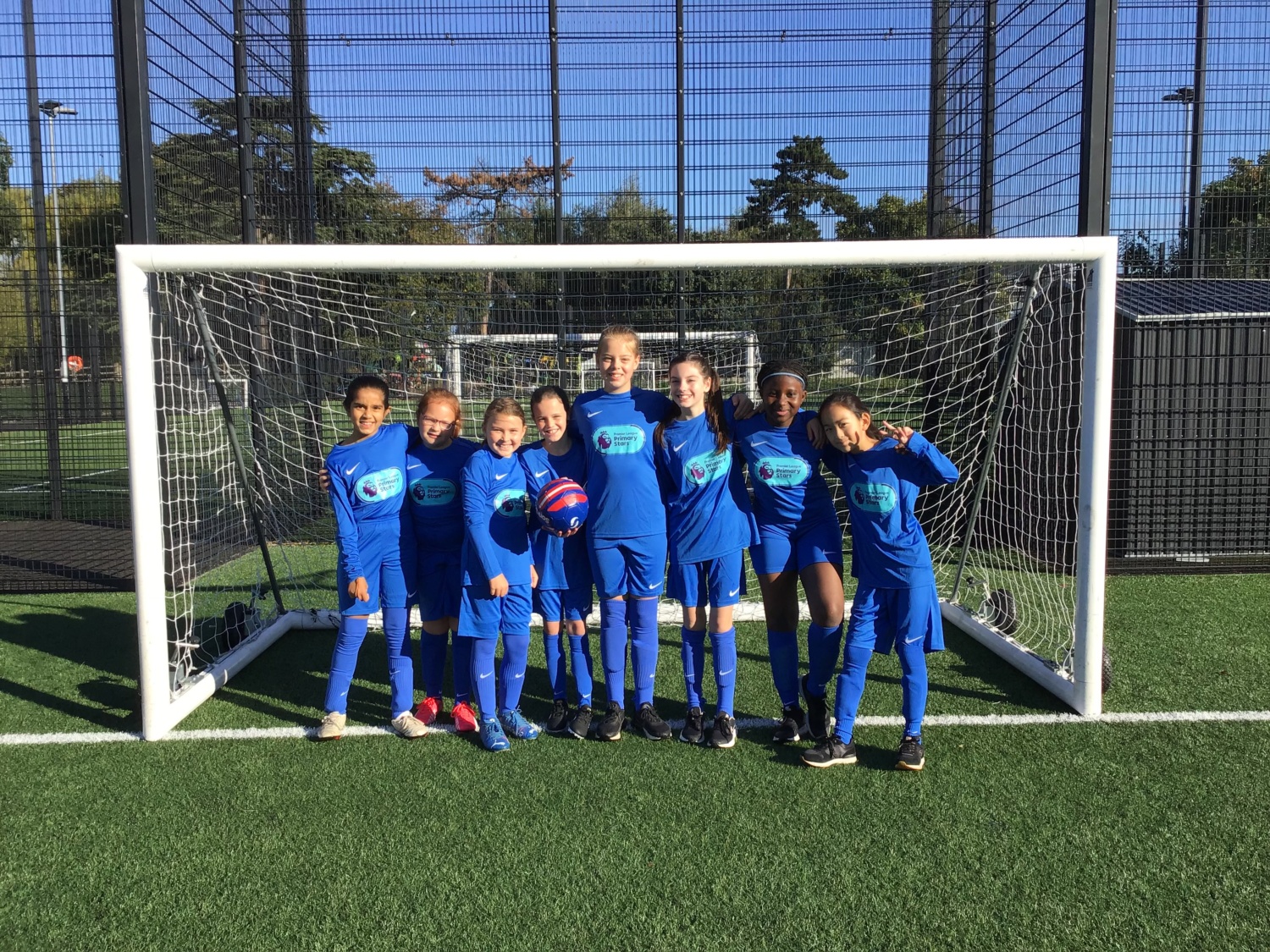 A team of 8 students in a blue kit, posing for a photo in front of a football goal