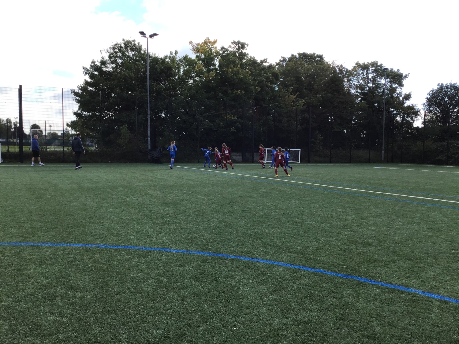 Two teams of students, in blue and red kits, playing football on a football pitch