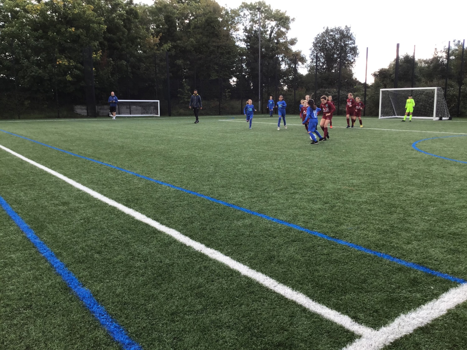 Two teams of students, in blue and red kits, playing football on a football pitch