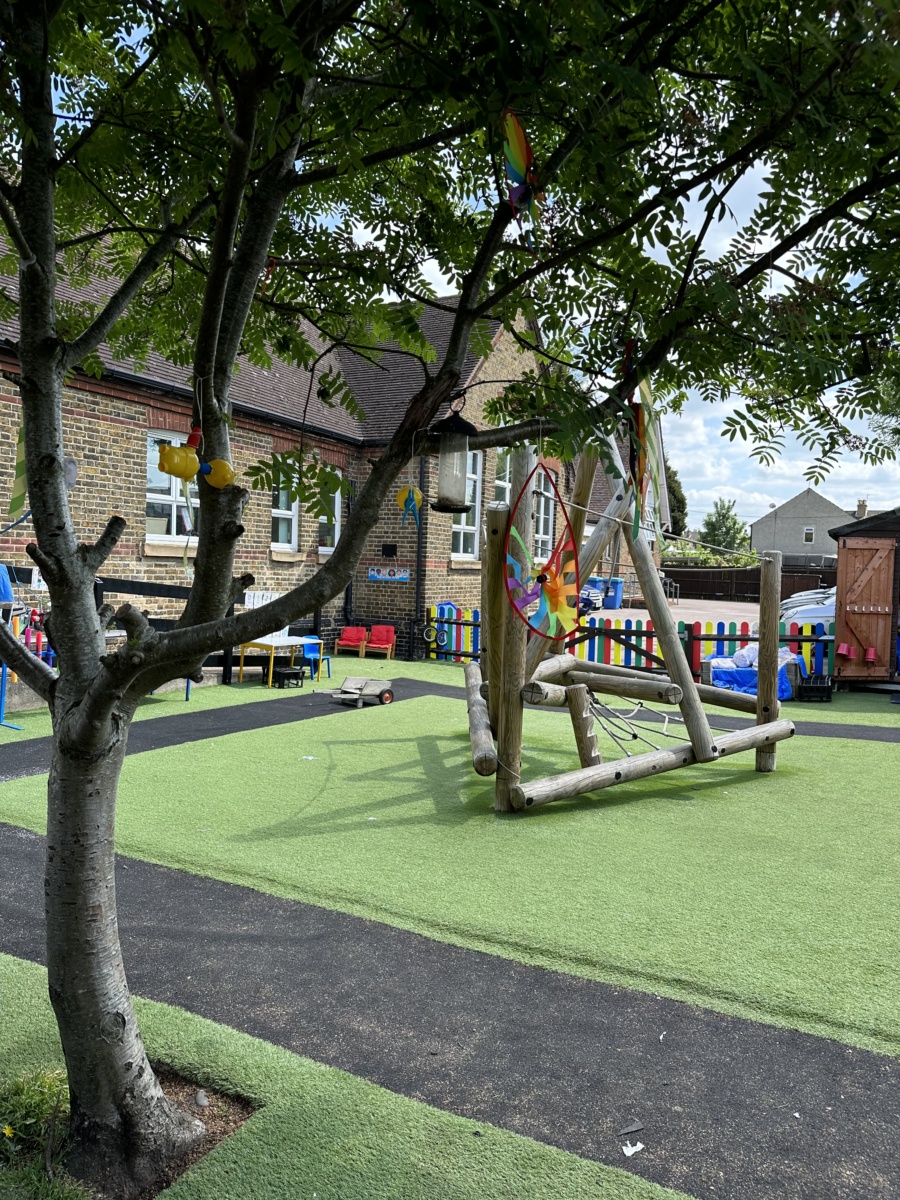 An image of the outdoor play area, with benches and a climbing frame, and a tree in the foreground