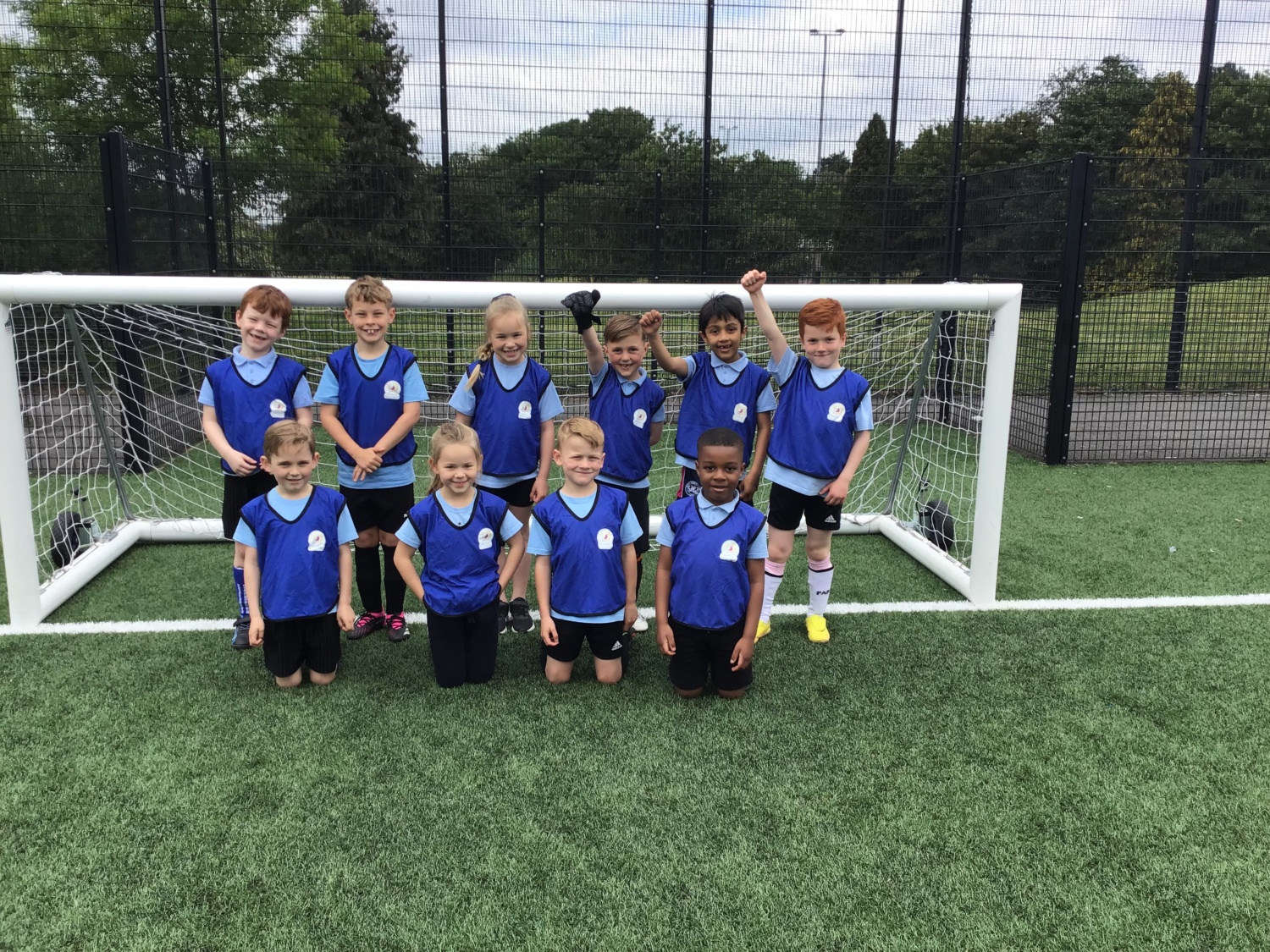 A team of children wearing blue, smiling for a photo in front of a goal