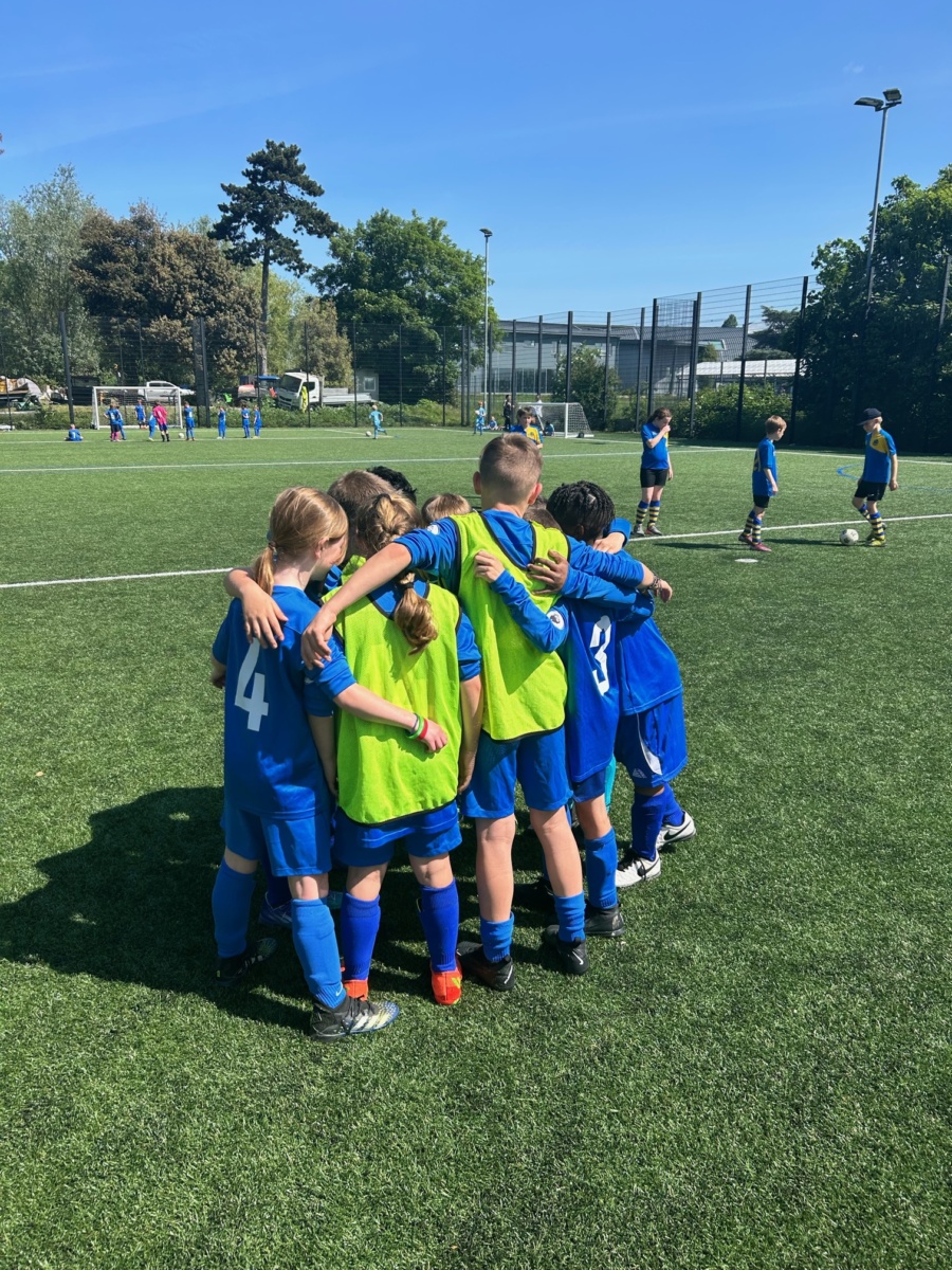 Years 3 and 4 pupils are pictured having a group hug on a grass pitch during a Football Festival they are competing in.