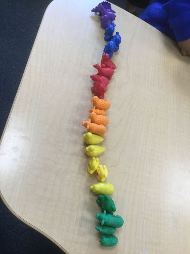 Some plastic farm animal toys are seen arranged in a line along a desk in colour order to make a pattern.