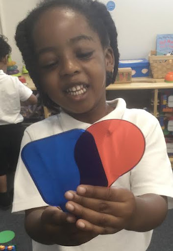 A young Nursery girl is seen experimenting with mixing different colours together, holding red and blue spades in her hands and smiling.