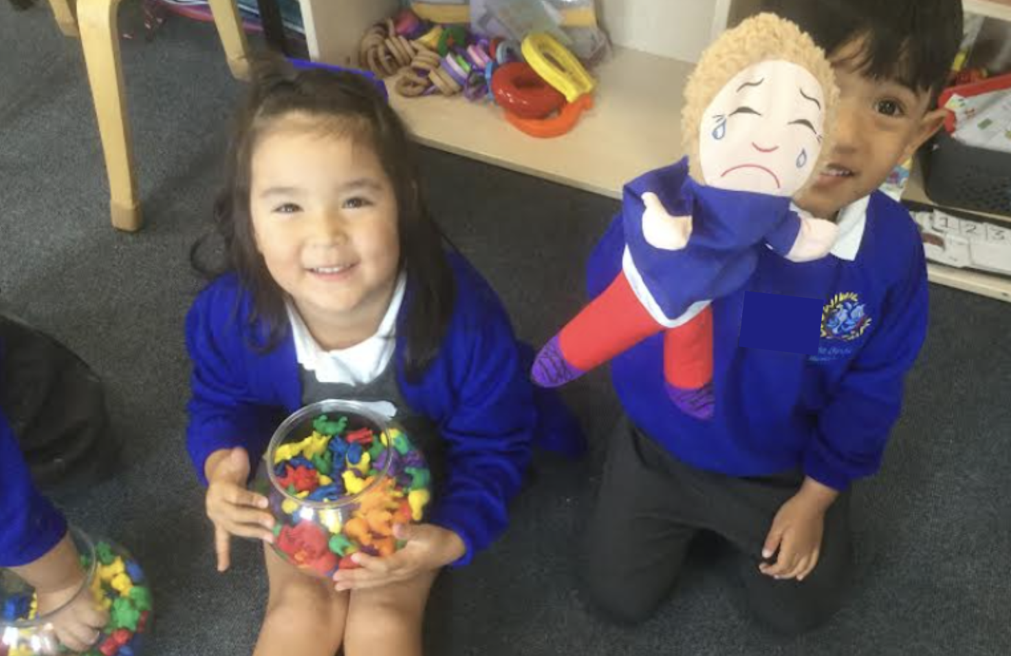 Two students sat on the floor holding toys and smiling for the camera.