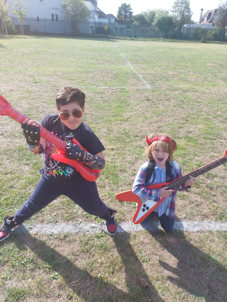 Two children, a boy and a girl, are seen dressed up as rockstars, holding inflatable guitars and posing for the camera.