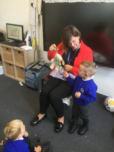 A young boy is shown interacting with a Rabbit soft toy, under the supervision of a member of staff at the front of the class.