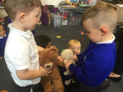 Two young boys are shown playing with soft toys together in a classroom.
