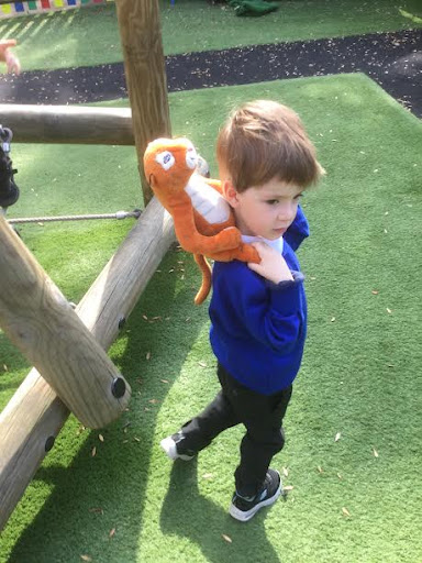 A young boy is shown holding a soft toy Tiger around his neck and playing in the school outdoor play area.