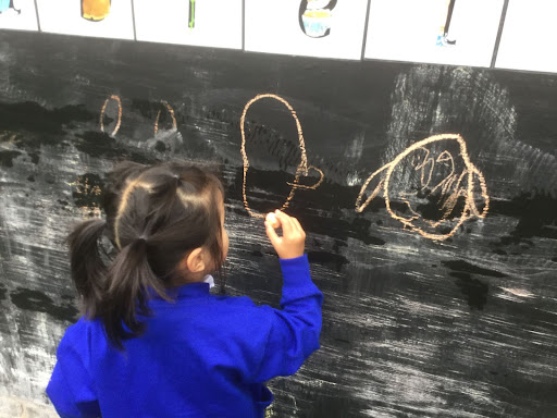 A young girl from Nursery is pictured drawing an Owl on the blackboard with some chalk.