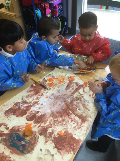 Four young pupils from Nursery are seen working together to create a piece of artwork inspired by the topic of Owls.