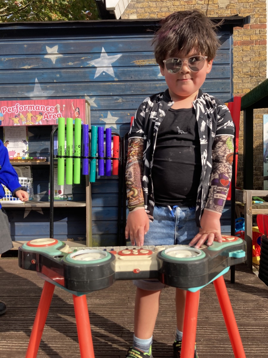 A child dressed up as a rockstar, stood behind a toy keyboard