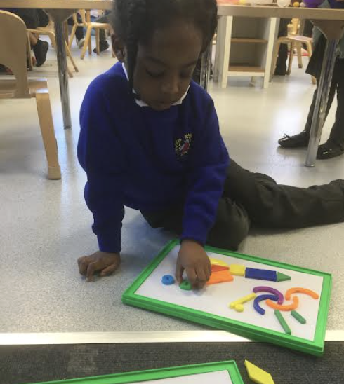 A young pupil is seen arranging coloured magnets on a whiteboard in the shape of fireworks.