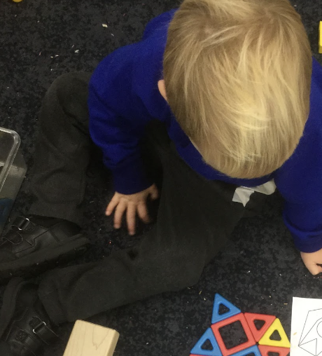A young pupil from Nursery is seen sat on the floor, playing with a puzzle.