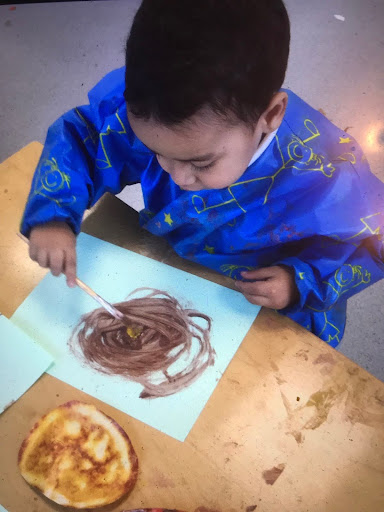 A young Nursery boy is seen wearing an apron whilst painting a picture inspired by the story of 'Chapatti Moon'.