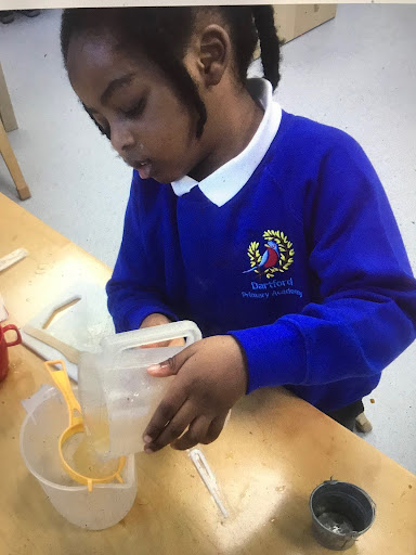 A young girl from Nursery can be seen making Orange Juice using jugs and a sieve.