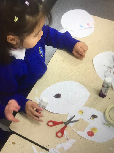 A young girl from Nursery can be seen using paper, scissors and glue to make some artwork inspired by the story of 'Chapatti Moon'.