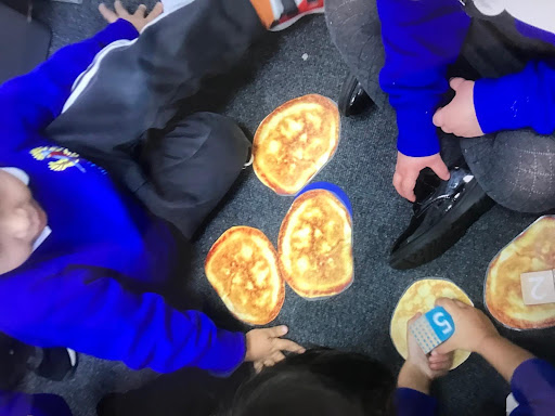 A small group of Nursery children are pictured sitting on the floor, about to eat some Chapattis.