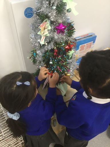 Two Nursery pupils are pictured decorating a Christmas Tree in their classroom together.
