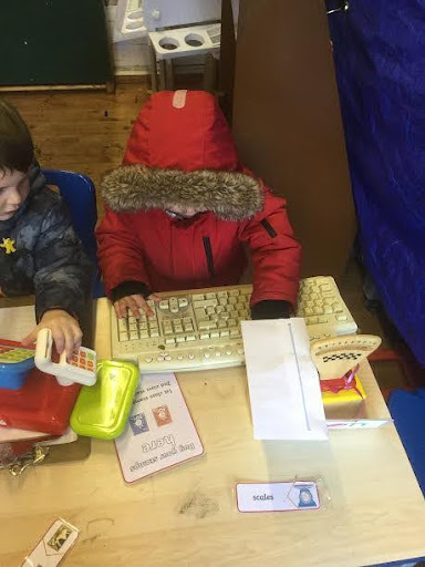 Two young Nursery pupils are pictured using keyboards and toy cash registers in their classroom.