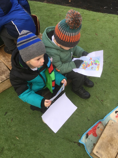 Two young boys from Nursery are pictured sat down outdoors in their winter clothing, observing maps.