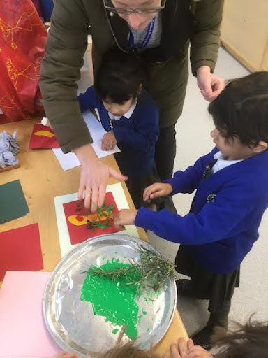 Photo showing two Nursery pupils using foliage collected from real trees in the garden, to print paint onto their own Christmas cards.