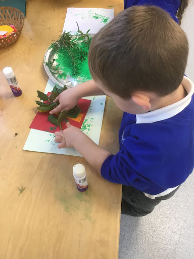 A young boy from Nursery is seen using foliage collected from real trees in the garden, to print paint onto Christmas cards he has made.