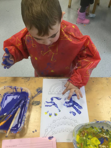 A young boy from Nursery is seen using his hands to make prints using coloured paint on a sheet of paper.