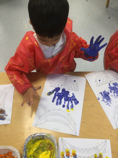 A young boy from Nursery is seen using his hands to make prints using coloured paint on a sheet of paper.
