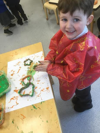 A young boy from Nursery is photographed wearing an art apron, whilst creating some artwork using plasticine.