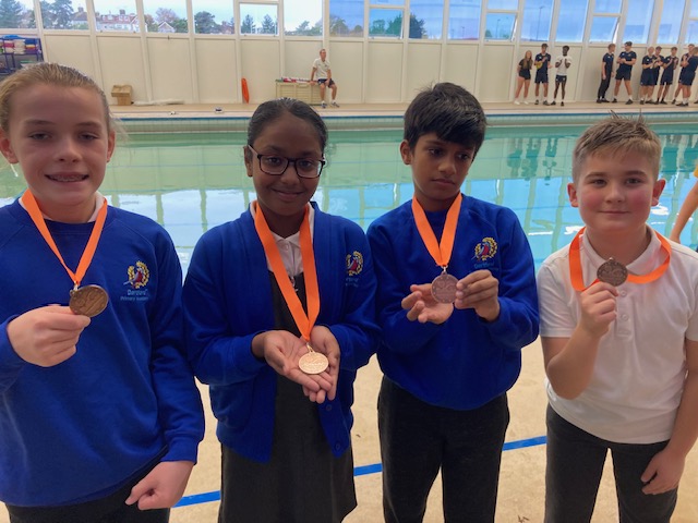 Four Dartford Primary Academy students are pictured smiling for the camera and holding up medals they have won at a swimming competition.