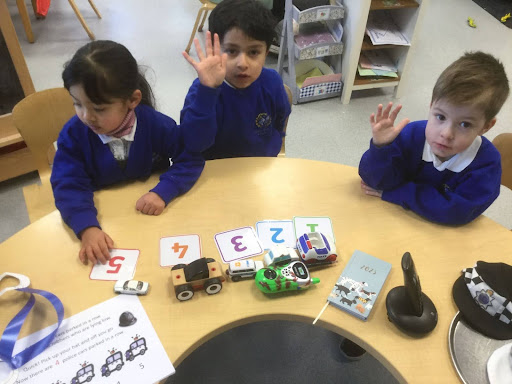 Three Nursery pupils, two boys and a girl are pictured sat together at a table, learning about counting numbers.