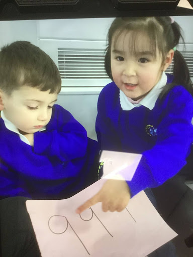 Two young Nursery pupils are seen using numbers written on sheets of paper to help them learn how to count.