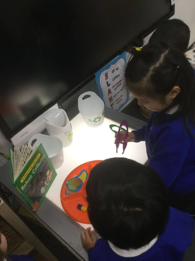 Two pupils from Nursery are pictured interacting with a lightbox to assist in their learning about refuse collection.