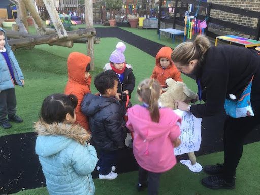 A group of Nursery pupils are pictured gathered together outdoors in their winter coats, listening to a member of staff who is speaking to them.