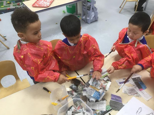 Four Nursery pupils are pictured wearing art aprons and using glue to create models out of newspapers.