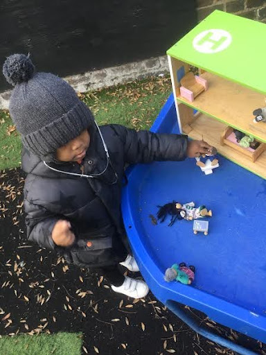 A young boy from Nursery is pictured playing with a toy house with figurines on an outdoor play area on the academy grounds.