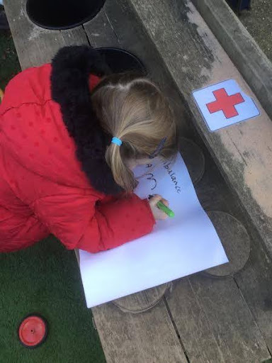 A young girl is seen writing with a pen on a sheet of paper outdoors on the academy grounds.