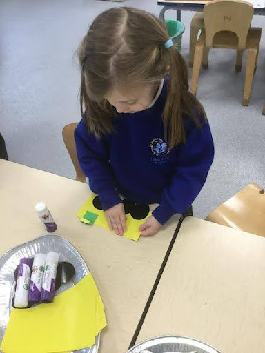 A young girl is seen gluing different coloured sheets of paper together with a glue stick during class.
