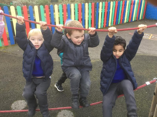Three Nursery pupils are pictured outdoors in their winter coats, climbing across a pair of ropes. Holding onto the top with their hands and walking across the bottom.