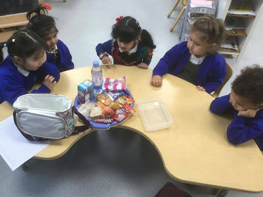 Five Nursery pupils are pictured sat around a table together, about to eat some food.