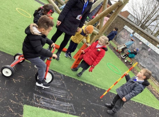 A small group of Nursery pupils are pictured playing together outdoors on the academy grounds, under the supervision of a member of staff.