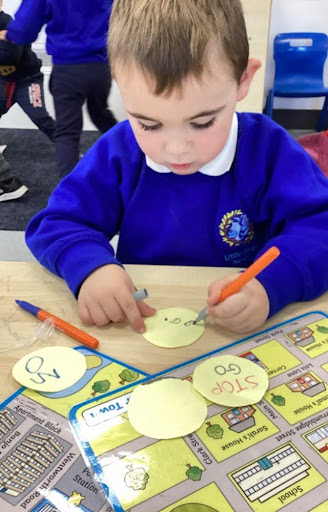 A young boy from Nursery is pictured sat at his desk, drawing road signs onto some circular pieces of paper.